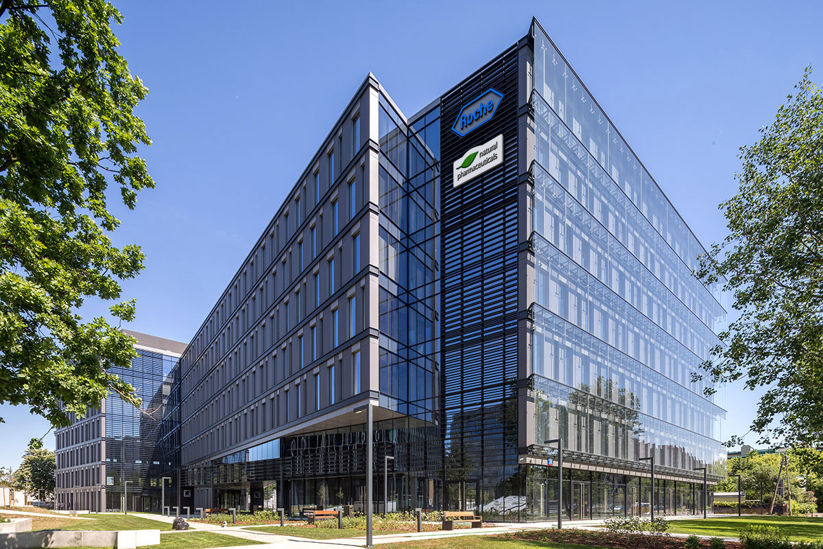 Natural Pharmaceuticals „VitaSolaris® D3“ Šiuolaikinis biurų pastatas su stikliniu fasadu saulėtą dieną.